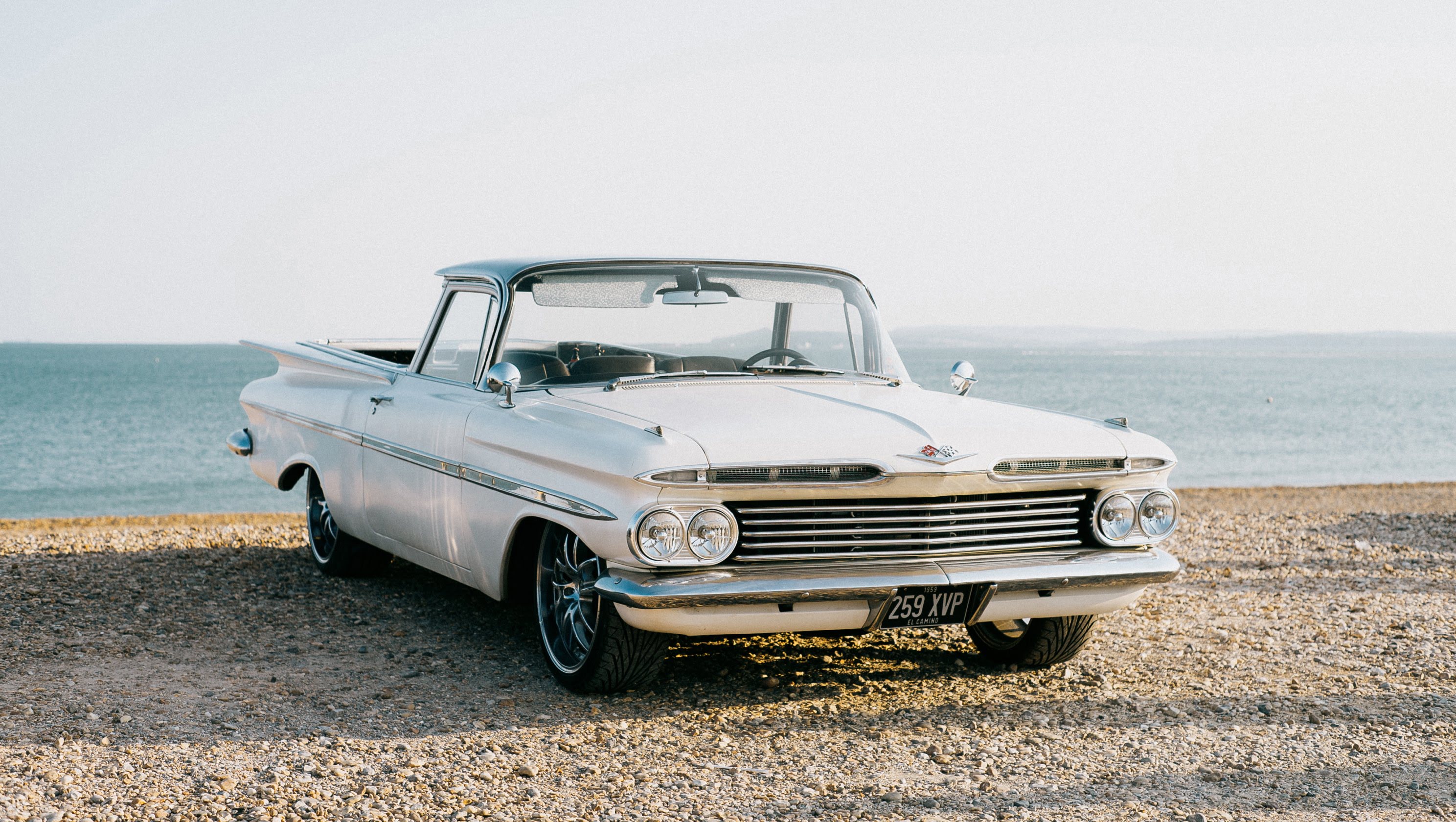 A landscape shot of a white classic car on the beach with the open ocean in the background