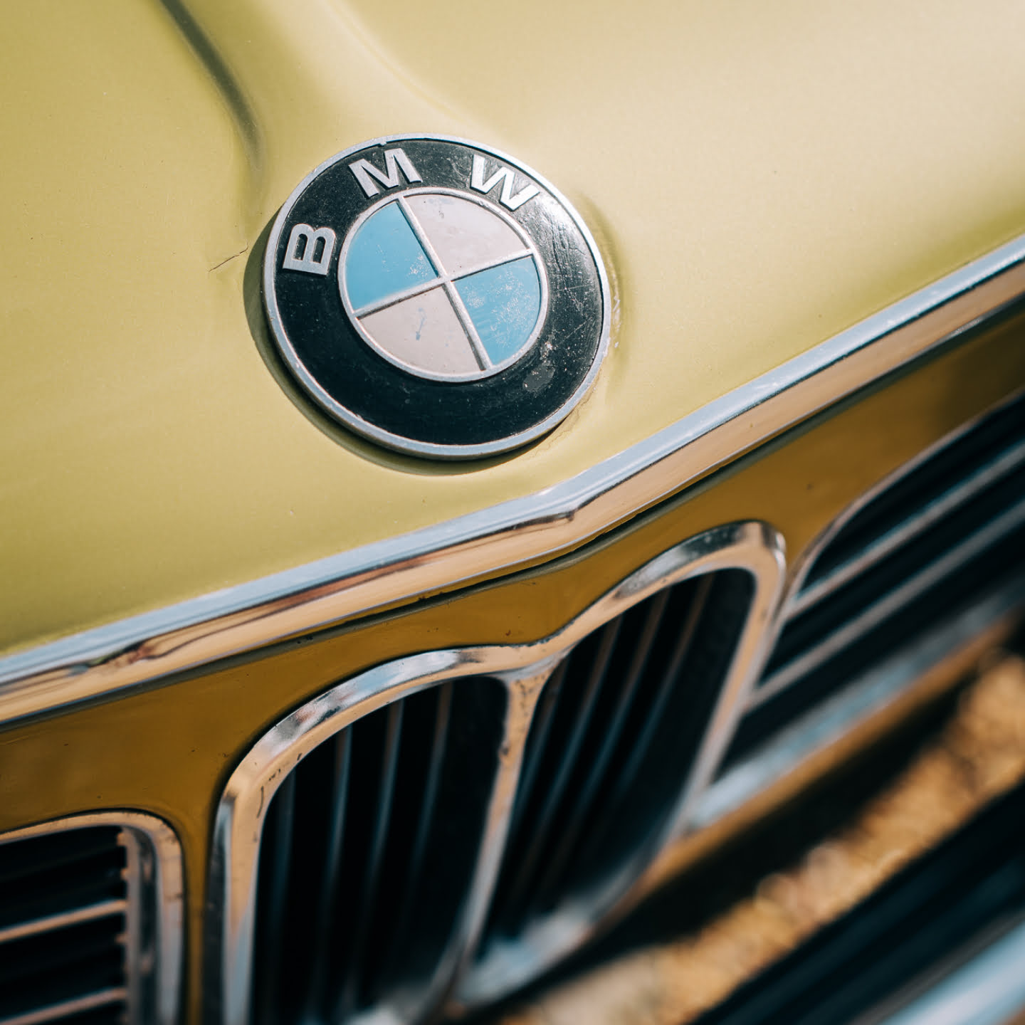 A close up of the front of a classic Yellow BMW, showing the badge in detail