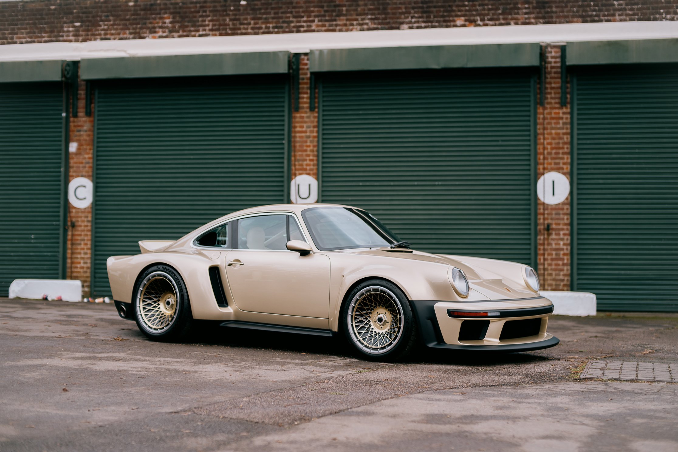 A landscape shot of a gold and black-trimmed Singer porsche 911